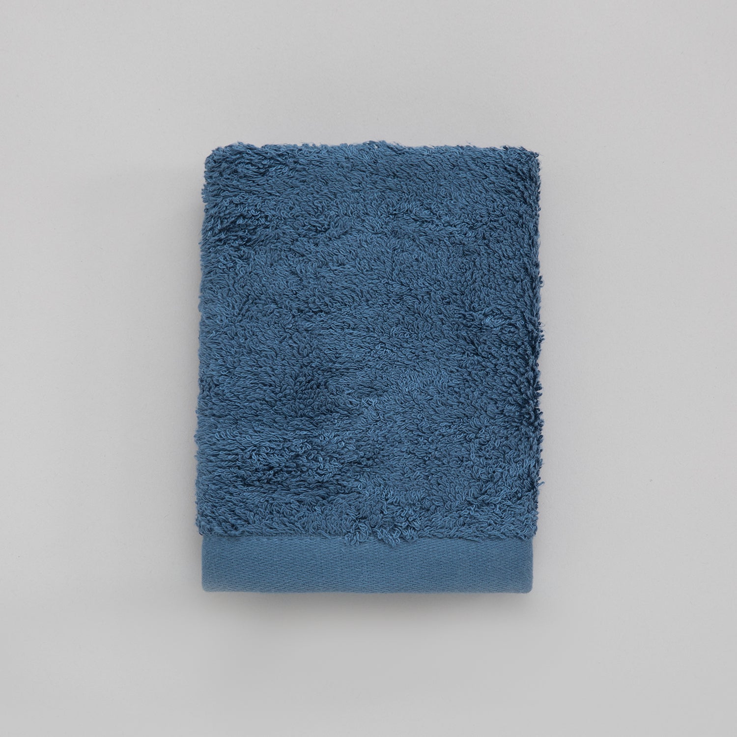 A solid blue colored guest towel made of cotton and bamboo, folded neatly on a flat surface.