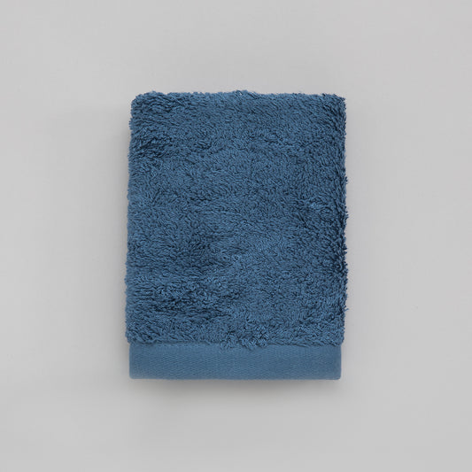 A solid blue colored guest towel made of cotton and bamboo, folded neatly on a flat surface.